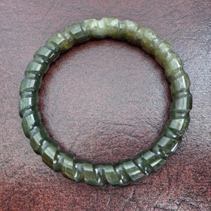May include: A green jade bangle bracelet with a twisted design. The bracelet is made of smooth, polished jade and has a natural, earthy look.