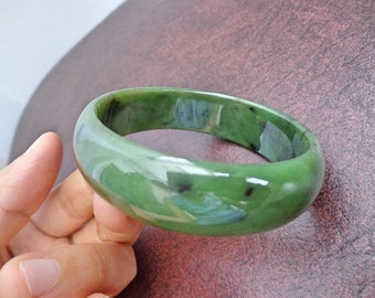 May include: A green jade bangle bracelet with black flecks. The bangle is smooth and polished.