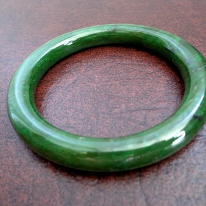 May include: A green jade bangle bracelet. The bracelet is smooth and polished, with a slight sheen.