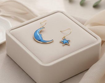 Brincos pendentes assimétricos em formato de lua crescente e estrela azuis, dourados.