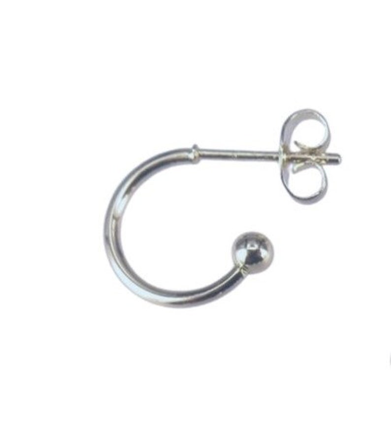 May include: A single silver-colored earring with a curved design. The earring features a small ball at the end of the curve and a post with a butterfly clasp for secure wear. The earring is set against a white background.