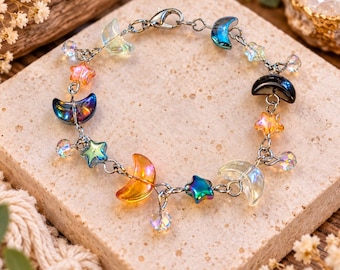 May include: A silver-toned chain bracelet featuring an array of charms shaped like crescent moons and stars. The charms are crafted from translucent and opaque glass in various colors including blue, orange, yellow, and black, with clear crystal beads.
