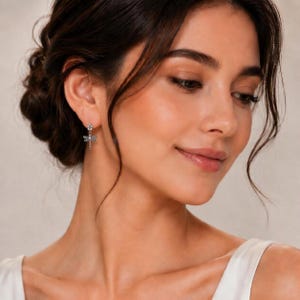 K&ouml;nnte beinhalten: Ein silberfarbener Ohrh&auml;nger mit einem kleinen blumenf&ouml;rmigen Stecker und einem zarten Libellenanh&auml;nger. Das Libellendesign ist mit kleinen, klaren Steinen besetzt, die auf der metallischen Oberfl&auml;che f&uuml;r ein dezentes Funkeln sorgen.