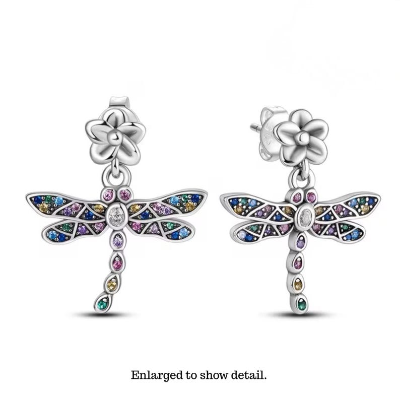 K&ouml;nnte beinhalten: Ein Paar silberfarbene Libellen-Ohrringe mit einem blumenf&ouml;rmigen Stecker. Die Fl&uuml;gel und der K&ouml;rper der Libelle sind mit kleinen, mehrfarbigen Edelsteinen in Blau-, Lila-, Rosa- und Gelbt&ouml;nen besetzt, mit einem klaren Stein in der Mitte.