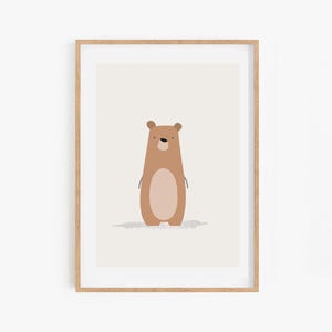 May include: A framed art print featuring a cartoon bear illustration. The bear is brown with a lighter brown oval belly and a small shadow. The artwork is set against a light beige background, framed in a natural wood frame.