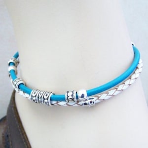 May include: A turquoise and white leather ankle bracelet with silver beads. The bracelet is braided and has a decorative design.