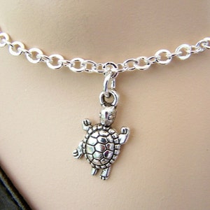 May include: A silver-colored necklace featuring a turtle pendant. The pendant is a detailed miniature turtle charm hanging from a delicate chain. The necklace is designed to be worn around the neck.