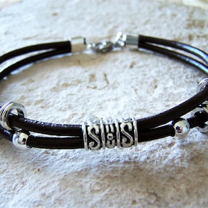 May include: A brown leather bracelet with silver beads and a silver charm with the word "SES" on it.