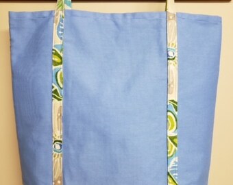 May include: A light blue tote bag with floral patterned fabric trim. The bag has two long straps and a white background with green and blue floral designs.