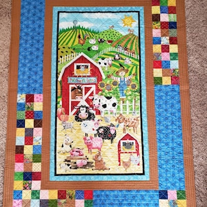 May include: A colorful patchwork quilt featuring a farm scene with a red barn, cows, pigs, and other farm animals. The quilt has a blue border with a repeating pattern and a brown outer border. The quilt measures approximately 60 inches by 80 inches.