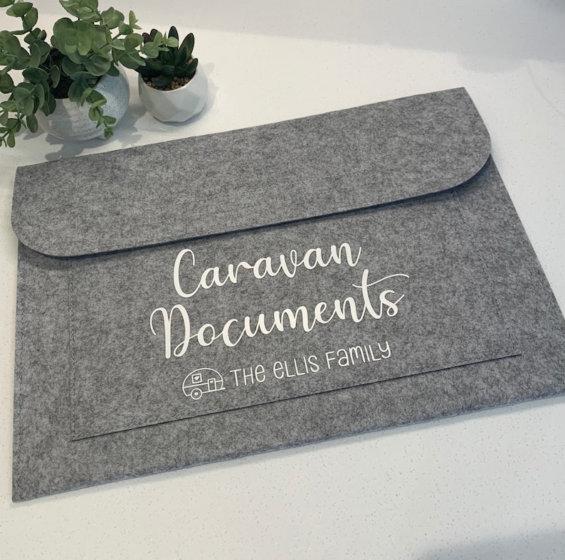 May include: Gray felt folder with the text "Caravan Documents" and "THE ELLIS FAMILY" in white lettering. A small white icon of a caravan is above the family name.