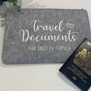 May include: Grey felt travel document pouch with white text that reads "Travel Documents The Protty Family". A blue passport is visible in the background.