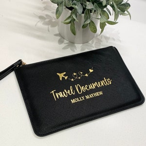 May include: Black travel document holder with a gold zipper and a gold airplane design with hearts. The text "Travel Documents" and "MOLLY MAYHEW" is printed in gold.