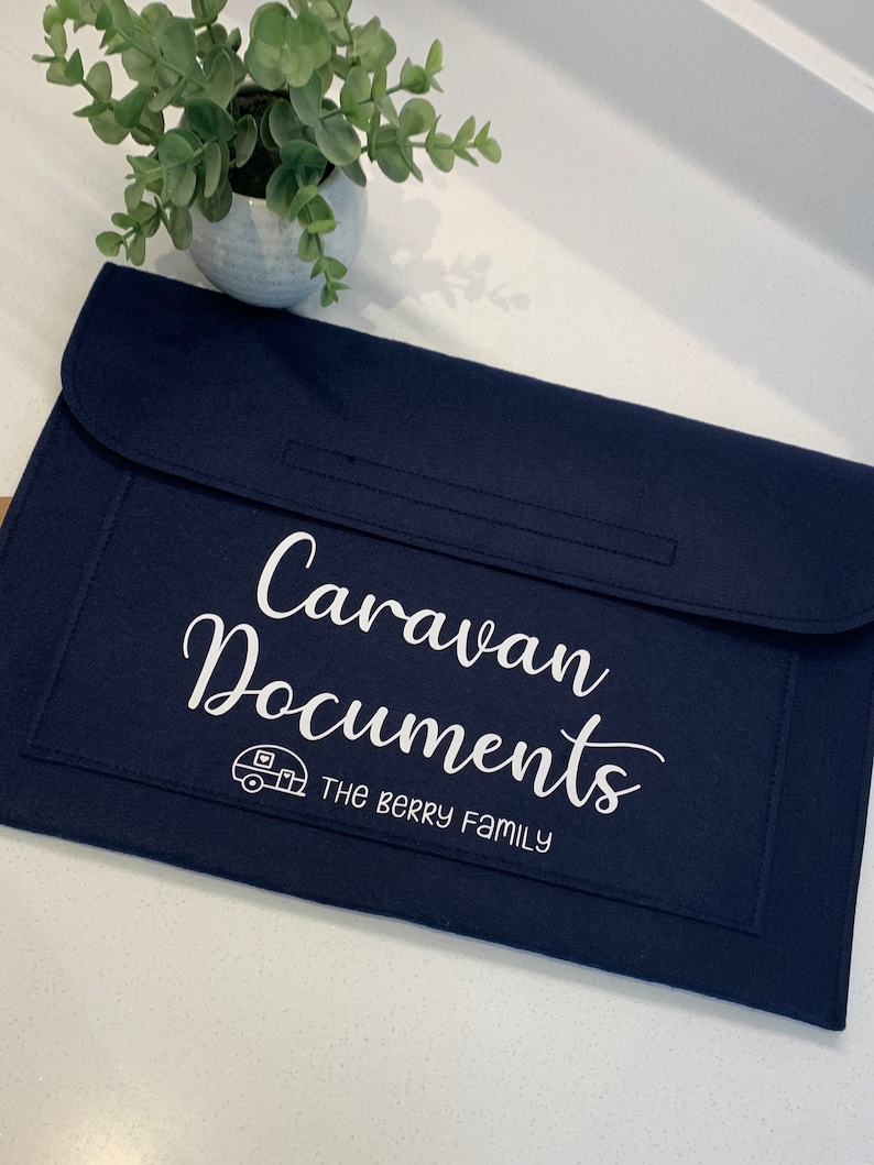 May include: A dark blue felt folder with a white embroidered design that says "Caravan Documents" and "The Berry Family". A small white caravan icon is also embroidered on the folder.