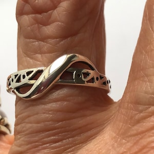 May include: A silver ring with a twisted design and intricate cutouts. The ring is worn on a finger.