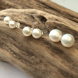 May include: Three pairs of pearl earrings in different sizes. The earrings are on a wooden surface.