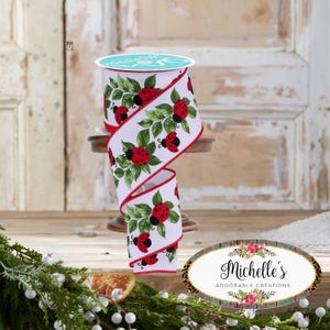 May include: A roll of white ribbon featuring a ladybug and leaf design. The ribbon has a red trim and is presented on a small wooden stand. The ladybugs are red with black spots, and the leaves are green.