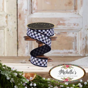 May include: A roll of black and white checkered ribbon with gold accents sits on a small wooden stand. The ribbon is displayed in a decorative swirl. The label on the ribbon spool reads "D. LUX".