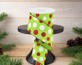 May include: A spool of lime green ribbon featuring a repeating pattern of large white polka dots and shimmering red glitter polka dots, with wired edges finished in a thin metallic red thread for structure and shape.