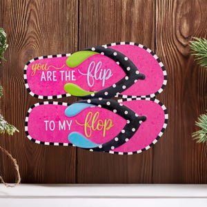 May include: Pink and black flip flops with white polka dots. The top flip flop says "You are the flip" and the bottom flip flop says "to my flop".