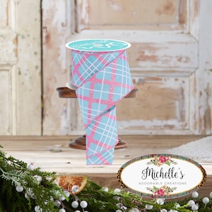 Könnte beinhalten: Eine Rolle dekoratives Band mit einem hellblauen und rosa Karomuster. Das Band wird auf einem kleinen Holzständer präsentiert. Das Band hat ein weißes Gittermuster über dem hellblauen und rosa Karomuster.