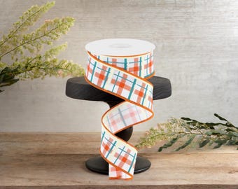 Peut inclure: Un rouleau de ruban blanc avec un motif à carreaux orange, bleu sarcelle et blanc. Le ruban est sur un support noir sur un fond en bois.