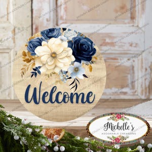 May include: A round wooden sign with the word "Welcome" in navy blue script. The sign is decorated with a floral arrangement in shades of white, navy, and gold. The sign has a rustic wood grain background. The sign is a decorative item.