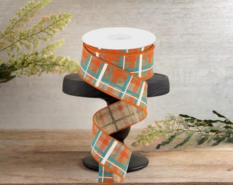 Peut inclure: Un rouleau de ruban à carreaux orange, brun et turquoise avec des accents blancs. Le ruban est enroulé autour d'une bobine blanche et repose sur un support noir.