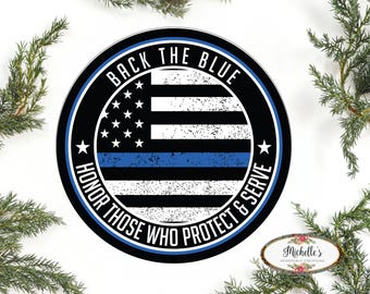 May include: A round, black and blue sticker with a thin blue line and an American flag. The text reads "Back the Blue Honor Those Who Protect & Serve".
