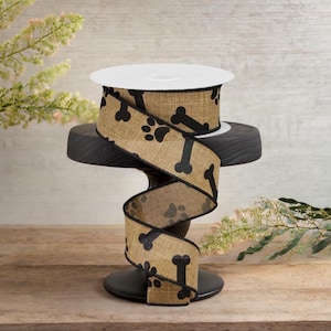 May include: A roll of brown burlap ribbon with black paw prints and bone designs. The ribbon is on a black stand.