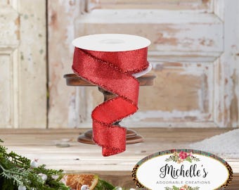 Puede incluir: Un rollo de cinta roja con purpurina se muestra sobre un pequeño soporte de madera. La cinta es de un rojo vibrante y festivo con una superficie texturizada y brillante. La cinta está dispuesta en un patrón decorativo y fluido, lo que sugiere su uso para manualidades o decoración navideña.