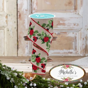 May include: A roll of decorative ribbon featuring a ladybug and leaf design. The ribbon has a natural linen background with red-edged borders. The ladybugs are red with black spots, and the leaves are green. The ribbon is displayed on a wooden stand.