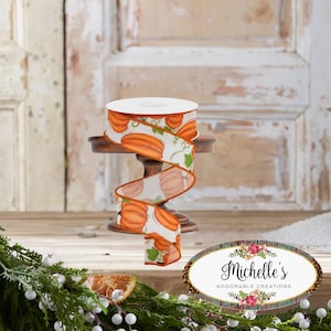 May include: A roll of decorative ribbon featuring a repeating pattern of orange pumpkins with green leaves on a white background. The ribbon is displayed on a small wooden stand, perfect for fall-themed crafts and decorations.