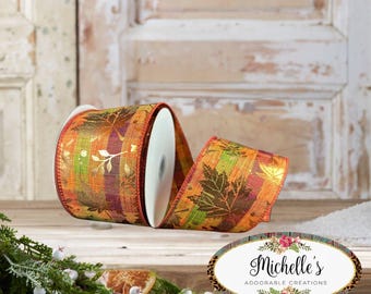 May include: A roll of wired ribbon featuring a plaid pattern in shades of orange, green, and purple, overlaid with metallic gold maple leaf silhouettes. An oval logo sticker with the text Michelle's ADORABLE CREATIONS is positioned nearby.