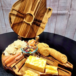 May include: A wooden serving board shaped like a spaceship, filled with snacks. The board holds crackers, cheese, carrots, chips, and a bowl of nuts and candies. The board is made of light and dark wood.
