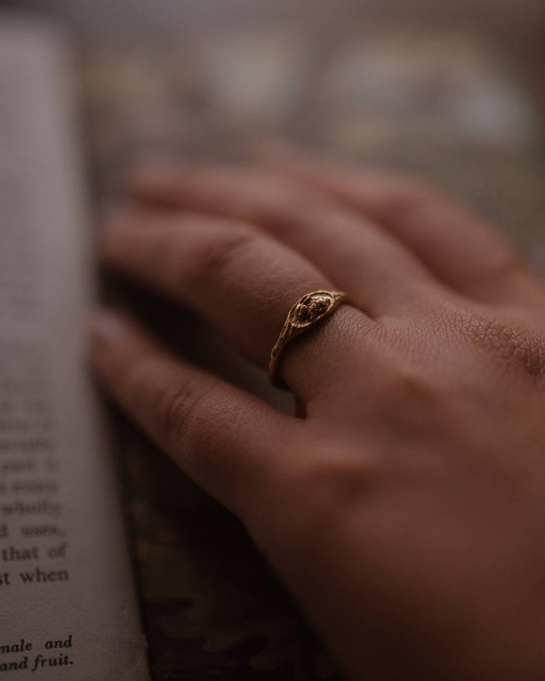 Pu&ograve; includere: Un anello d'oro con un designo testurizzato sulla fascia. L'anello &egrave; indossato su un dito.