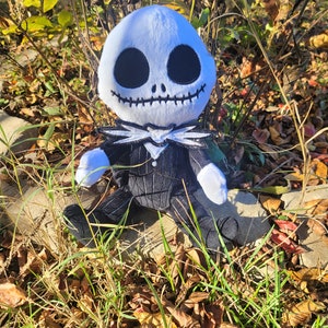 May include: A plush toy of Jack Skellington from the Nightmare Before Christmas movie. The toy is wearing a black and white striped suit with a white collar and bow tie. The toy is sitting on a bed of brown leaves.
