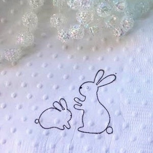 Mama and baby bunny image hand stamped on beverage size napkins in white with raised dots to provide texture. Mama bunny is sitting up with hands outreached to the baby bunny. The bunnies are facing each other.