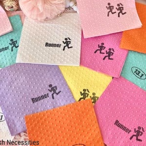 May include: A collection of colorful, textured napkins in shades of pink, orange, green, yellow, and purple. Each napkin features a runner graphic and the word "Runner" or the number "13.1".