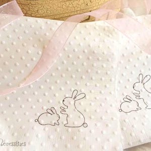 May include: White napkins with a dotted texture and bunny illustrations. The napkins have a pink ribbon and are suitable for Easter or spring celebrations. The text "Selfish Necessities" is visible in the bottom left corner.
