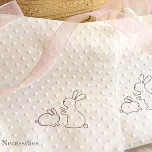 May include: White napkins with a dotted texture and bunny illustrations. The napkins have a light pink ribbon and are suitable for Easter or spring celebrations. The napkins have a simple, elegant design.