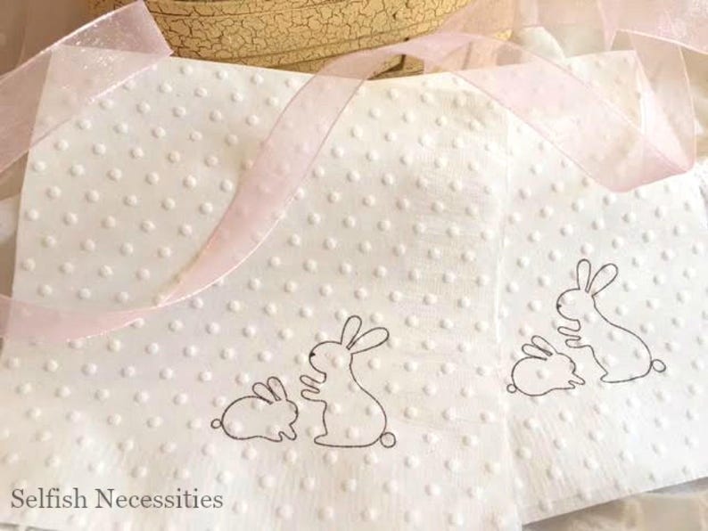 May include: White napkins with a dotted texture and bunny illustrations. The napkins have a light pink ribbon and are suitable for Easter or spring celebrations. The napkins have a simple, elegant design.