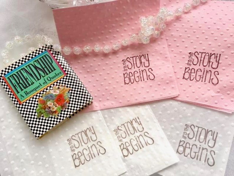 May include: Four white napkins with the text "and the story begins" printed in brown ink. Two pink napkins with the same text printed in black ink. A small black and white checkered book titled "Friendship, A Bouquet of Quotes".