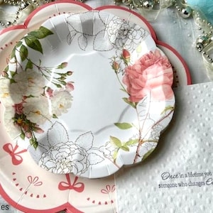 May include: Two pink and white floral paper plates with scalloped edges. The top plate features a pink rose and the bottom plate features a white rose. The text "Once in a lifetime you meet someone who changes Everything" is printed on a white napkin.