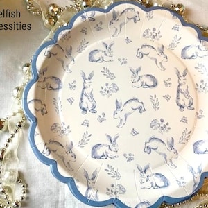 May include: Blue and white paper plates with a scalloped edge and a pattern of bunnies and flowers. The text "Selfish Necessities" is printed on the top of the plate.