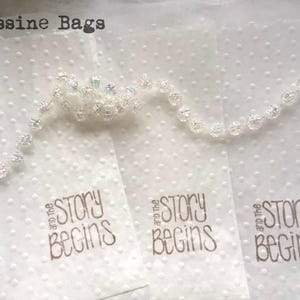 May include: Three white, translucent, glassine bags with a dotted pattern. Each bag has the text "and the story begins" printed in gold.