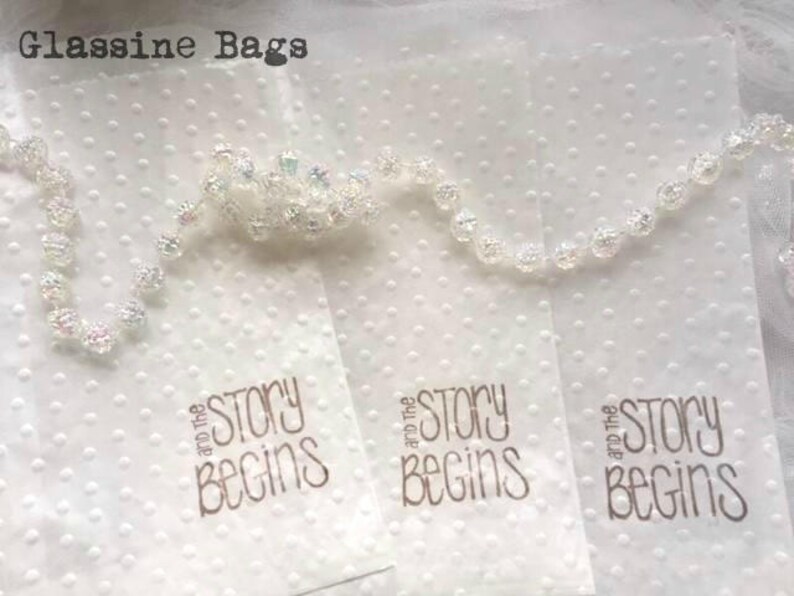 May include: Three white, translucent, glassine bags with a dotted pattern. Each bag has the text "and the story begins" printed in gold.