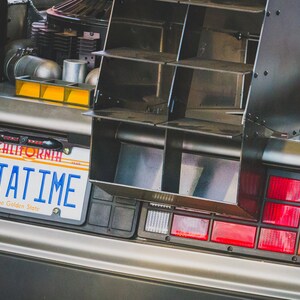 May include: A silver car with a California number plate that reads "OUTATIME" and a black rear spoiler. The car has a red and orange rear light.