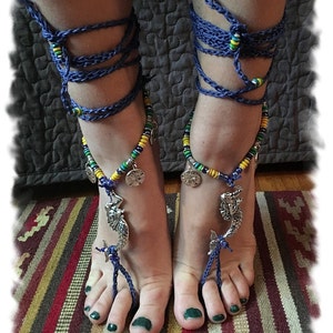 May include: Blue and green beaded ankle bracelets with silver mermaid charms. The bracelets are tied around the ankles with blue cords.