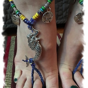 May include: A blue and yellow beaded anklet with a mermaid charm and two starfish charms. The anklet is worn on a person's foot with green nail polish.